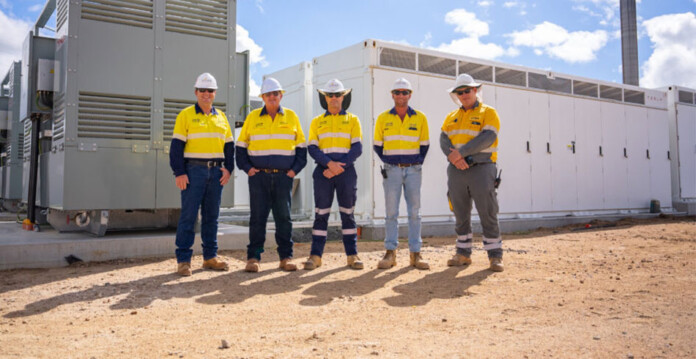 Stanwell employees pose for photo in front of battery units wearing hard hats and high-vis workwear